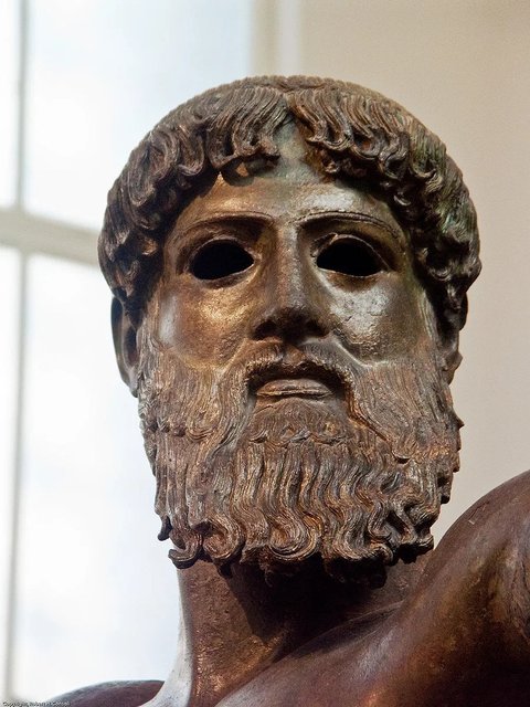 The head of the Artemesium Bronze is an exquisite piece of ancient Greek sculpture. Face is that of an adult male, bearded and stern. The figure's hair is stylized yet detailed. The beard is also rendered meticulously. The facial expression is serious, and arguably somewhat ambiguous. The eyes of the statue are hollow, given the statue a lifelike gaze.