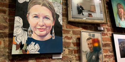 Three framed paintings and two photographs hanging on a brick wall