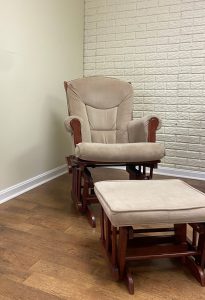 A reclining chair sits in the corner of an empty room with white walls and a wood floor.
