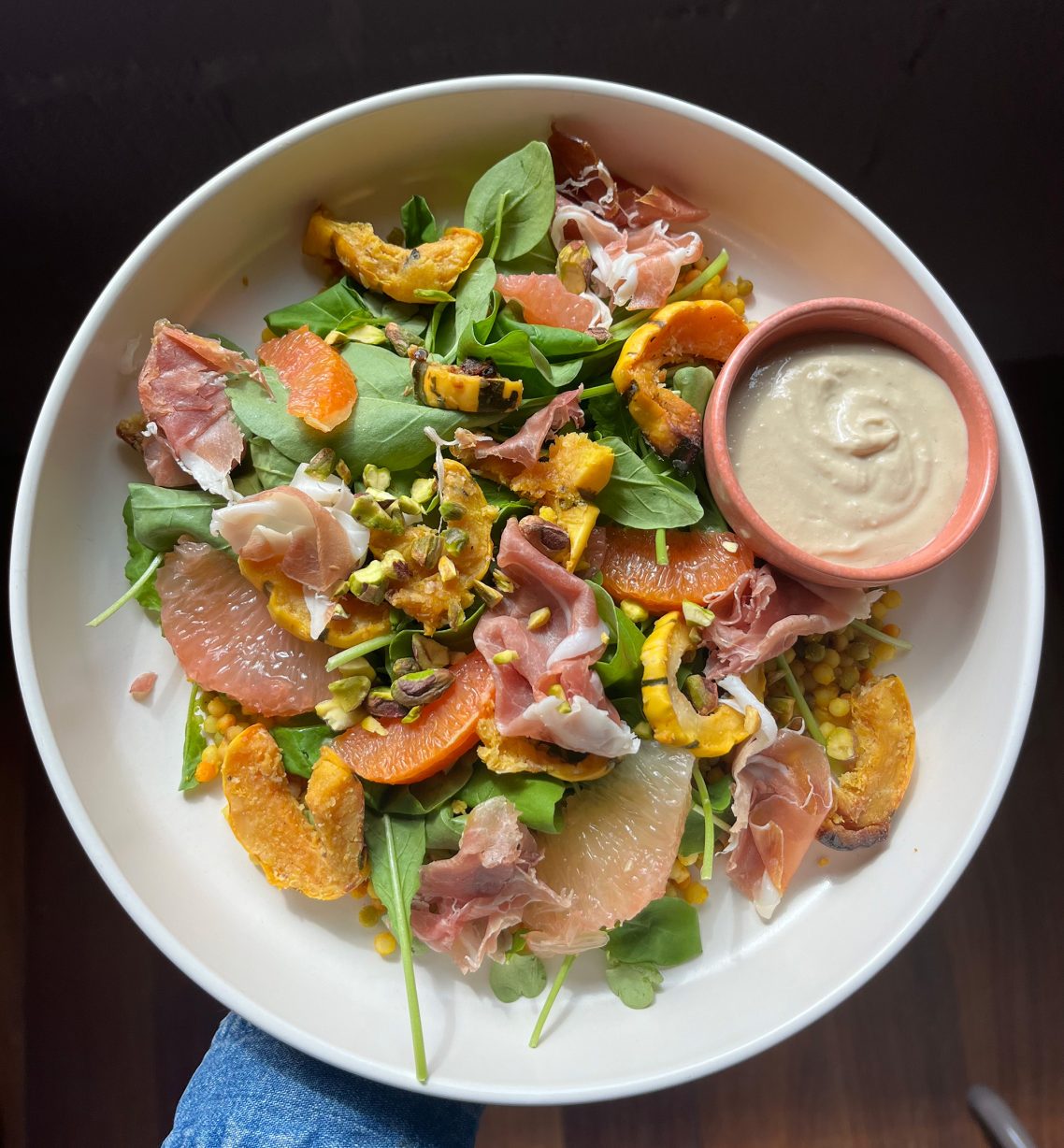 A ceramic bowl filled with greens, orange slices and ham