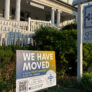 A sign saying "we have moved" outside an old, stately white house.