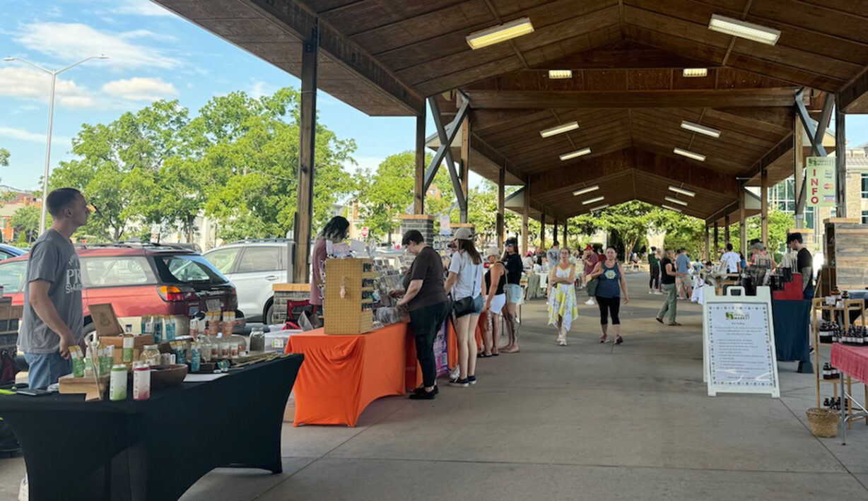 People walking past tables with food and goods