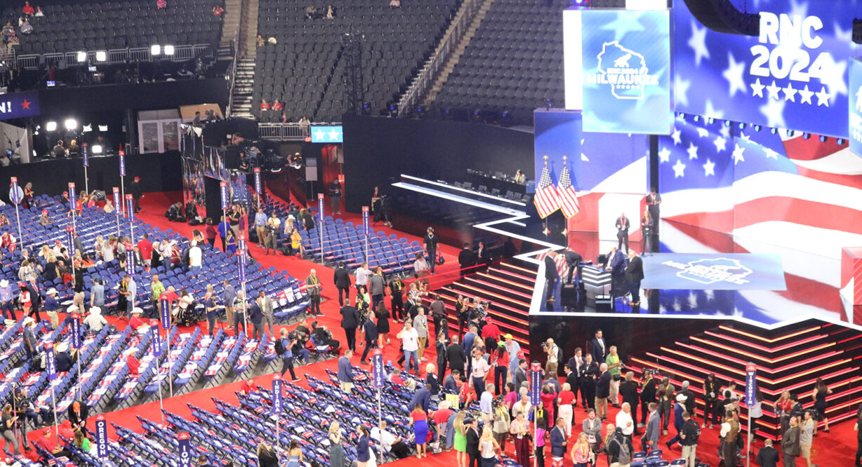 people standing around empty seats in front of a big stage with a digital screen