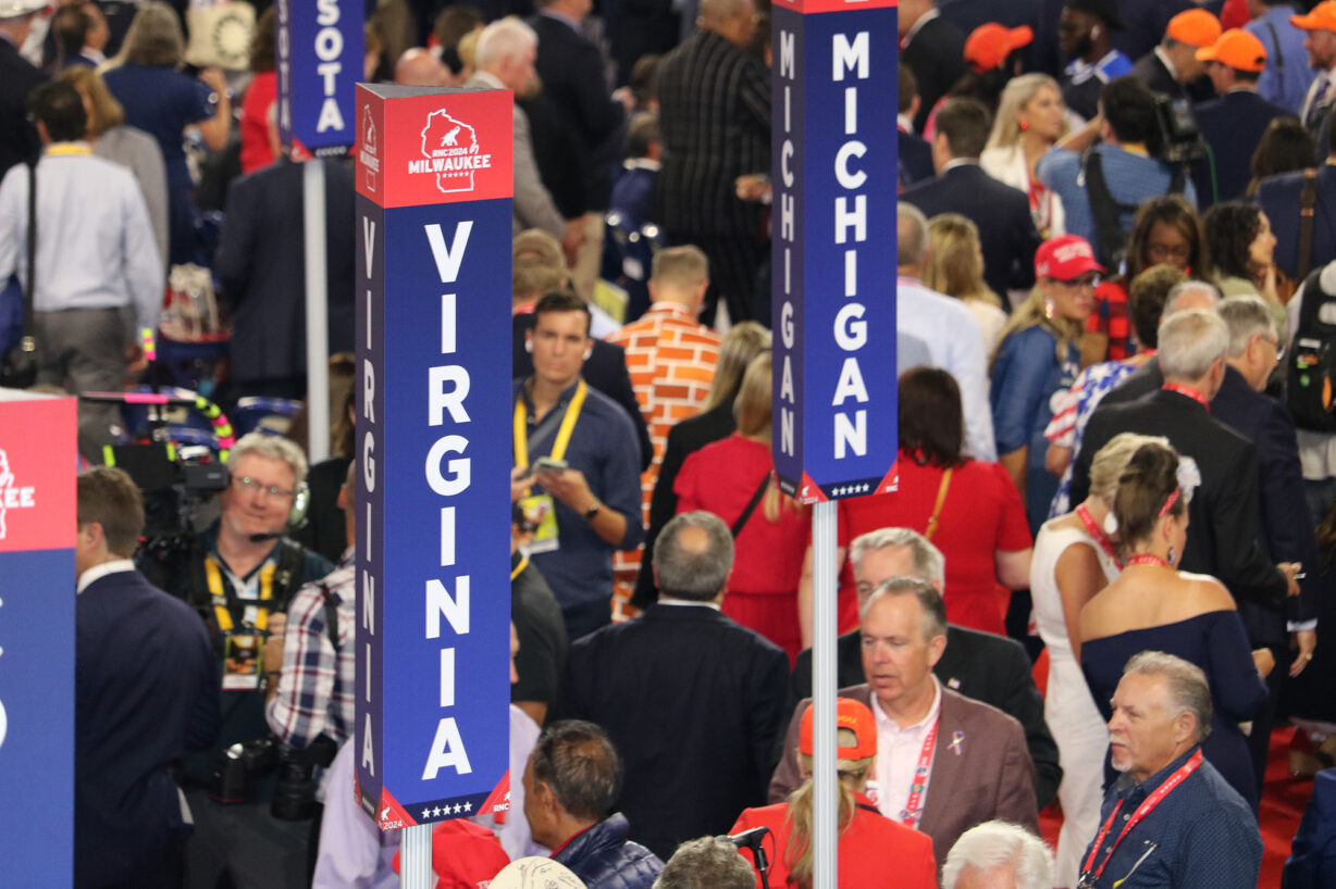 A sign saying "Virginia" spelled vertically with people milling around