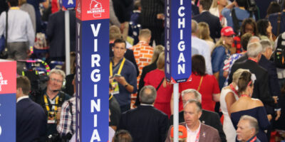 A sign saying "Virginia" spelled vertically with people milling around