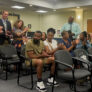 Four people standing while two dozen others sitting clap