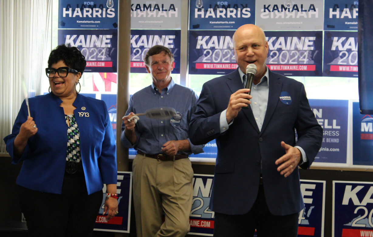 A woman and two men stand in front of blue and white campaign signs.