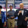 A woman and two men stand in front of blue and white campaign signs.