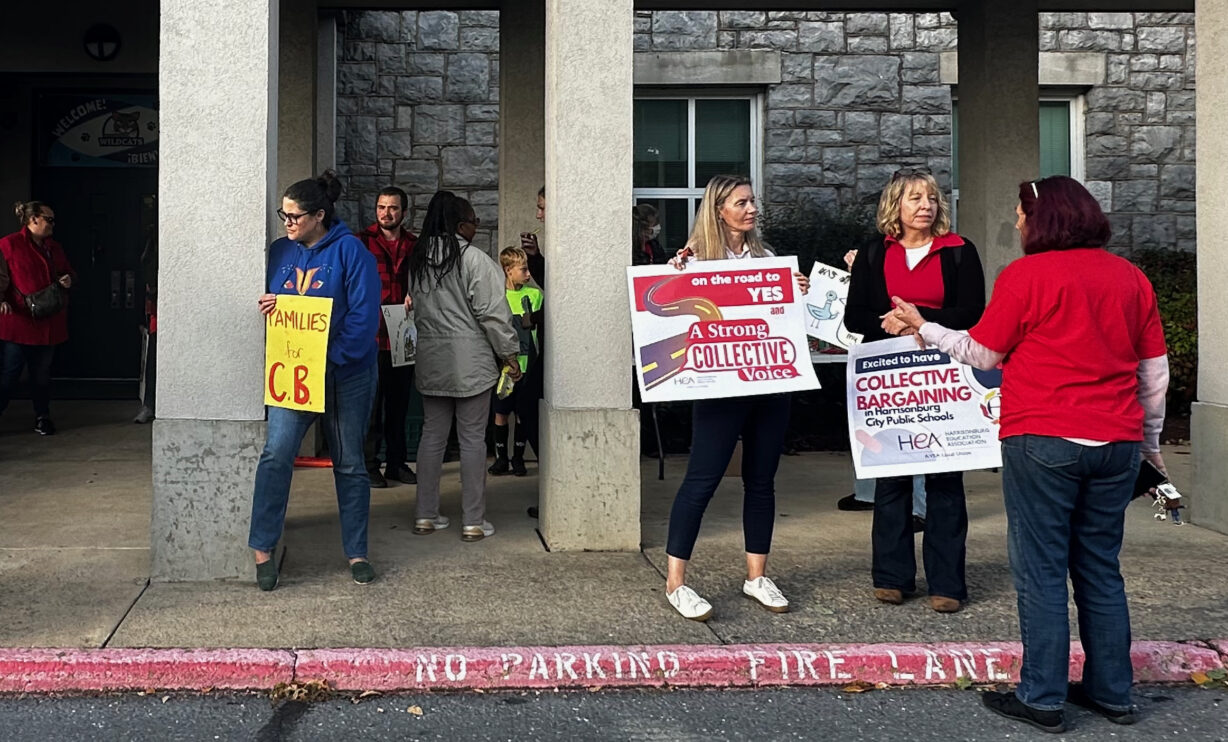 People holding signs saying "A strong collective voice" and "Families for CB" outside a school building.