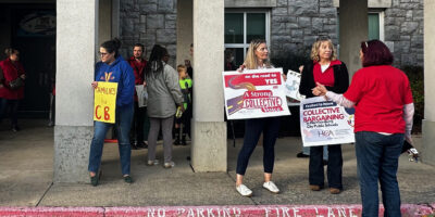 People holding signs saying "A strong collective voice" and "Families for CB" outside a school building.