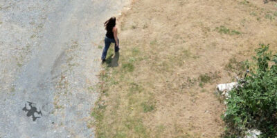 A photo taken from above showing a shadow of a drone behind a woman.