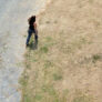 A photo taken from above showing a shadow of a drone behind a woman.