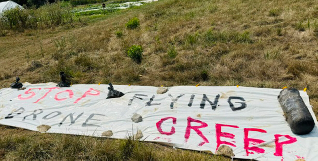 A hand-painted sign laid across the ground that says "stop flying drone creep"