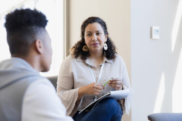 Image Credit: iStock; Description: The counselor listens to the young adult and takes notes for their next meeting.