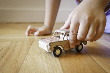 This is a nostalgic image of a young boy playing with an antique toy SUV on a wood floor.