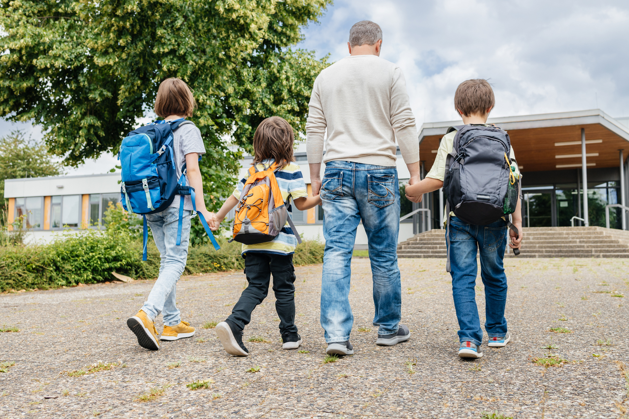 View from the back of a happy parent who escorts his children sons and daughter to school. Back to school. Father's care for children.