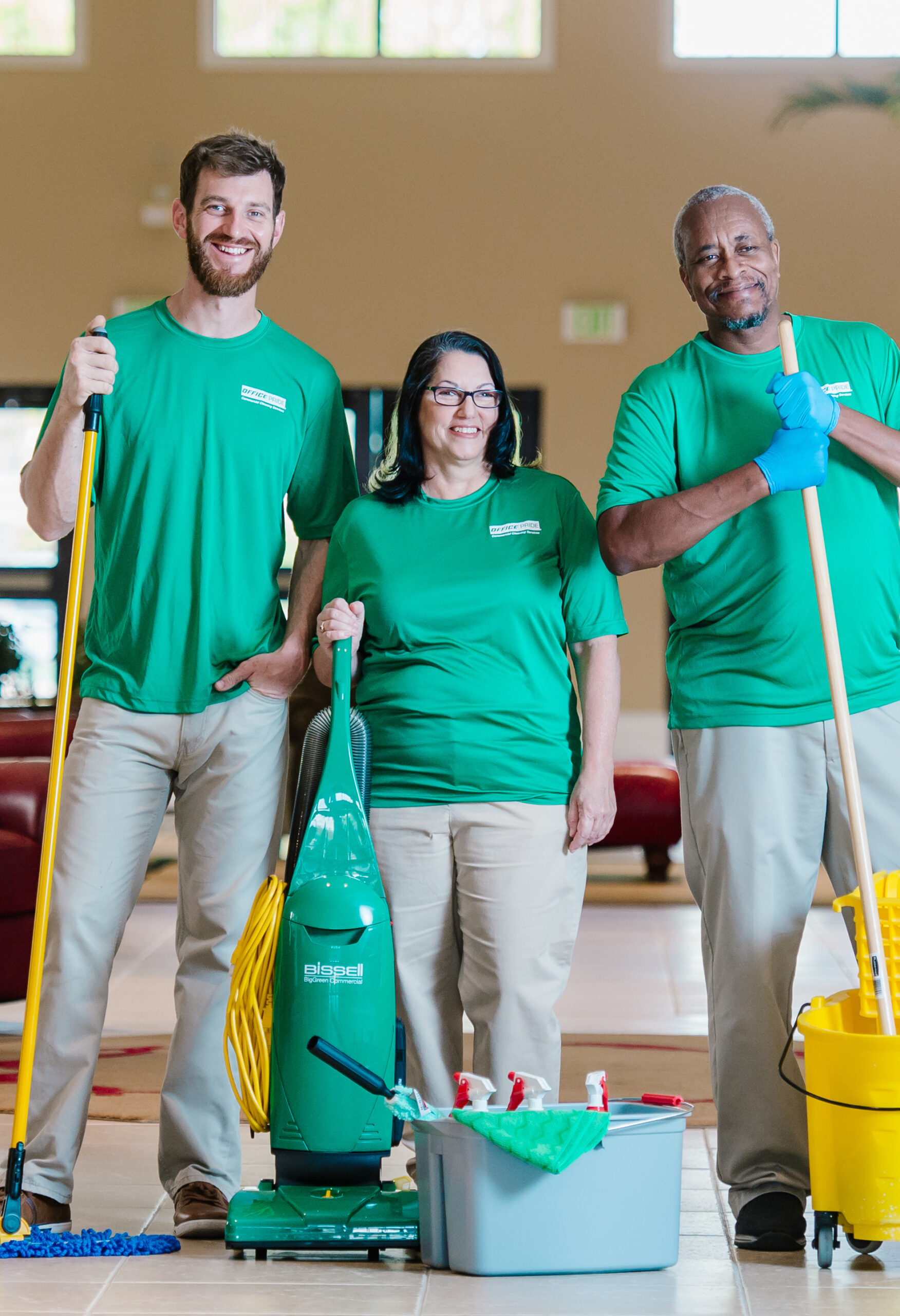 commercial cleaning team posing with duster, vacuum and mop in bucket