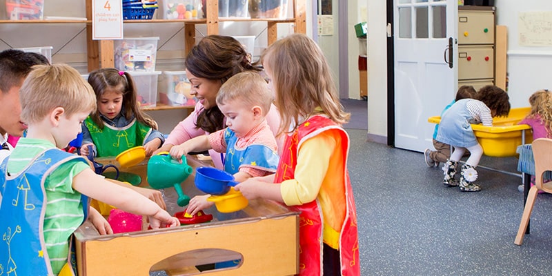 preschool student picking toy tools out of a container while an instructor explains the activity