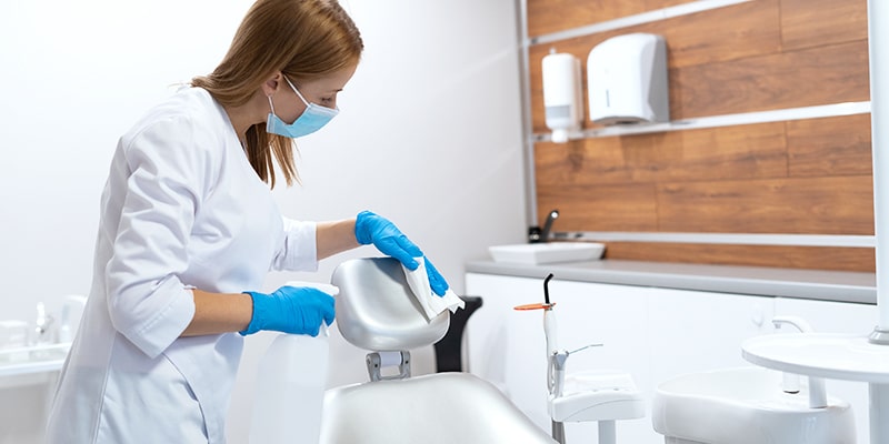 a cleaning professional wipes the headrest of patient chair with a cleaning solution