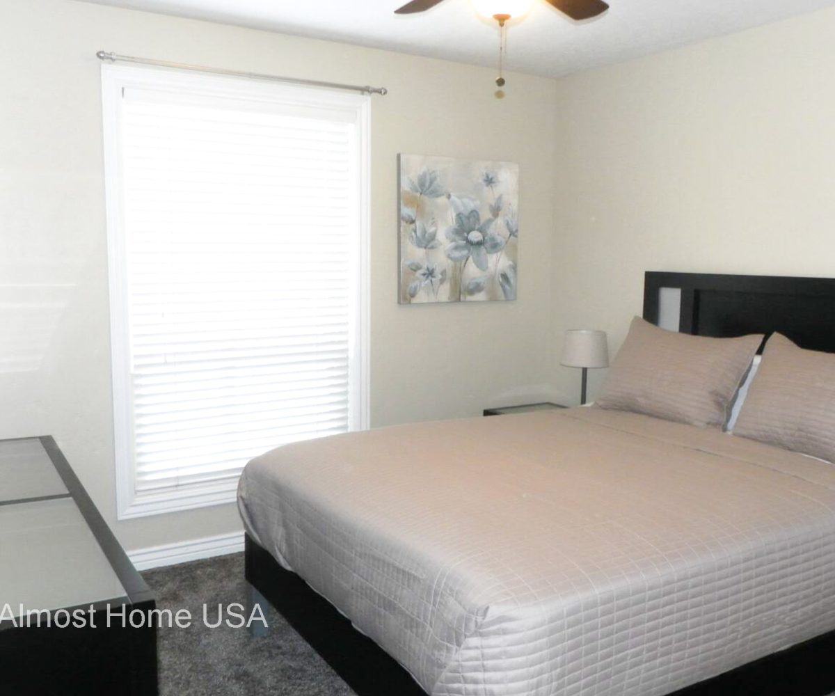 Queen bed and large window in bedroom located in furnished home in Sandy Utah.