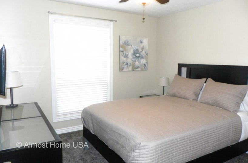 Queen bed and large window in bedroom located in furnished home in Sandy Utah.
