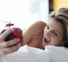 angry woman holding alarm clock in bed