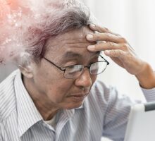 An older Asian man staring at a cell phone with lost memory and dementia