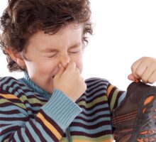 School age boy holds his nose with one hand and trainer shoe in the other