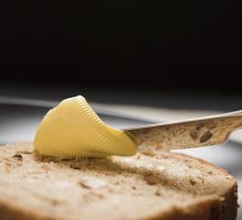 A slice of brown granary bread being spread with butter