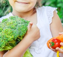 young girl holds colorful veggies