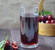 cold cherry juice in a glass and pitcher on wooden table with ripe berries in wicker basket