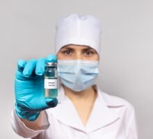 Masked and gowned individual holds out measles vaccine