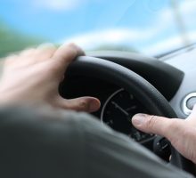 Over shoulder view of a man driving a car with his hands on the steering wheel turning quick