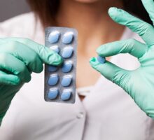 woman in white coat and medical gloves holds blue Viagra pills to prevent Alzheimer's Disease