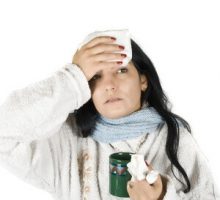 a woman with the flu or a cold holds tissues and a cup of tea