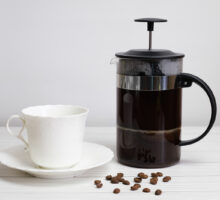cup and saucer, coffee beans and French press for preparing unfiltered coffee