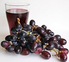A glass of grape juice beside freshly washed grapes.