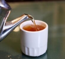Tea pouring from spout of metal tea cup into white cup, no handle, Chinese style