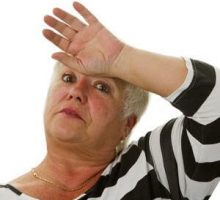 an older woman with her hand on her forehead having a hot flash
