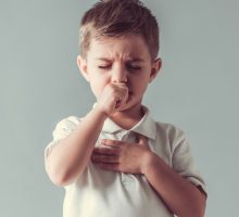 young boy coughing and holding chest