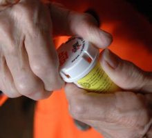 someone trying to remove the child proof safety cap from a bottle of prescription pills