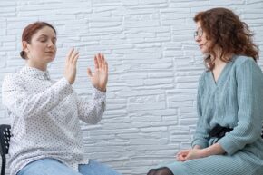 Psychotherapist in blue dress conducts hypnosis session for female patient in white shirt