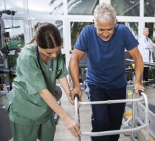 Nurse Assisting Senior Man To Walk Using Walker at a Rehab Hospital