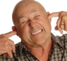 man with tinnitus plugs his ears with his fingers in frustration