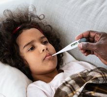 Sick child in bed with grandmother taking her temperature to determine if she needs children's fever medicine