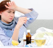 sick woman lying in bed surrounded by lots of cold and flu remedies