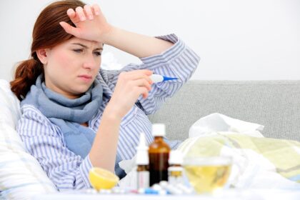 sick woman lying in bed surrounded by lots of cold and flu remedies