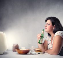 woman eating a burger and drinking a beer in front of the television
