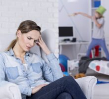 mother in foreground looks defeated, child climbing over bed in background; what we get wrong about ADHD
