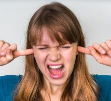 Woman closes ears with fingers because ears ring with tinnitus as an adverse reaction to COVID vaccines
